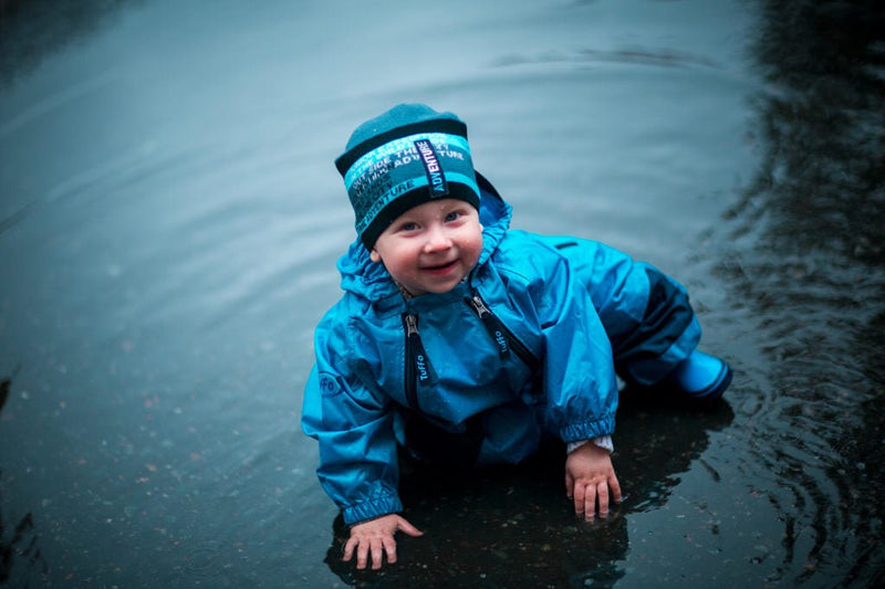 Happy little boy splashing in water puddle while wearing Blue Tuffo Muddy Buddy Mountain Kids Canada rain suit.